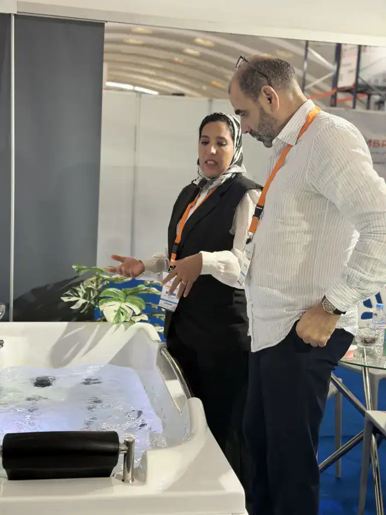 PoolSPA à Africa Pool & Spa Expo 2026 : le bien-être à la rencontre des professionnels 12 Femme en gilet noir échangeant avec un visiteur près d’une baignoire de balnéothérapie sur le stand PoolSPA.
