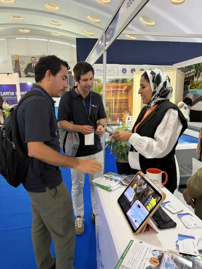 PoolSPA à Africa Pool & Spa Expo 2026 : le bien-être à la rencontre des professionnels 16 Femme en gilet noir présentant des supports à deux visiteurs, avec une tablette posée sur le comptoir PoolSPA.